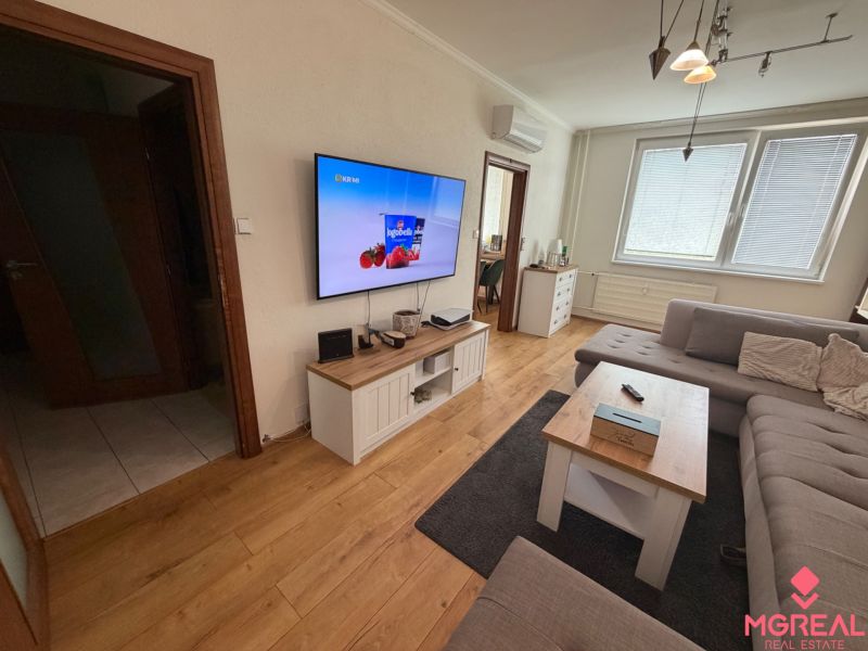 Living room with wood-patterned flooring, gray sofa, and television, in a three-room apartment.
