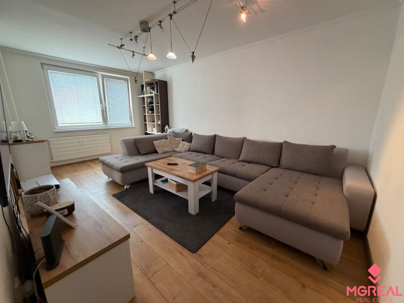 Living room with a large sofa, coffee table, and wooden decor flooring in a 3-room apartment.