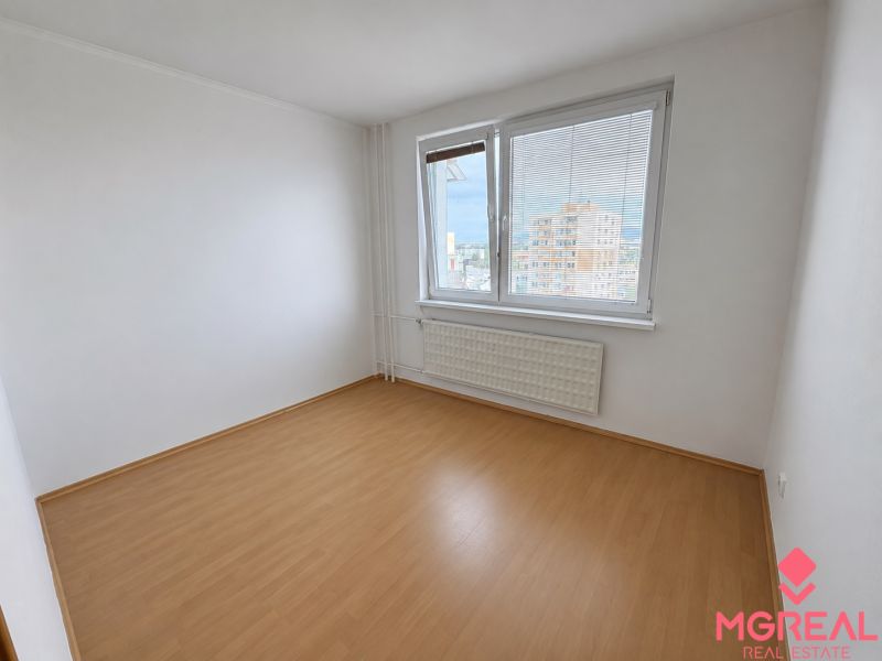 A room in a 2-room apartment with a wooden decor floor, a large window, and a radiator.