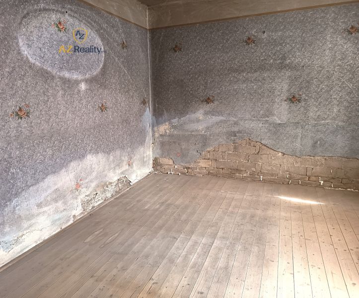 An empty room with peeling plaster and a wooden-patterned floor in a family house.
