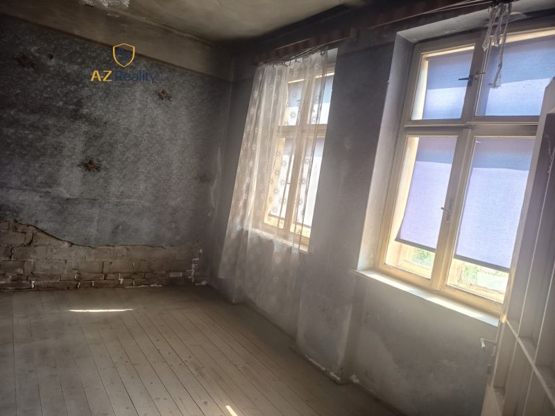Interior of a family house with wooden flooring, unrenovated walls, and windows with curtains.