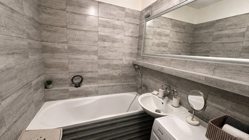 A bathroom with a bathtub, sink, and washing machine in a 3-room apartment. Gray tiles dominate the space.