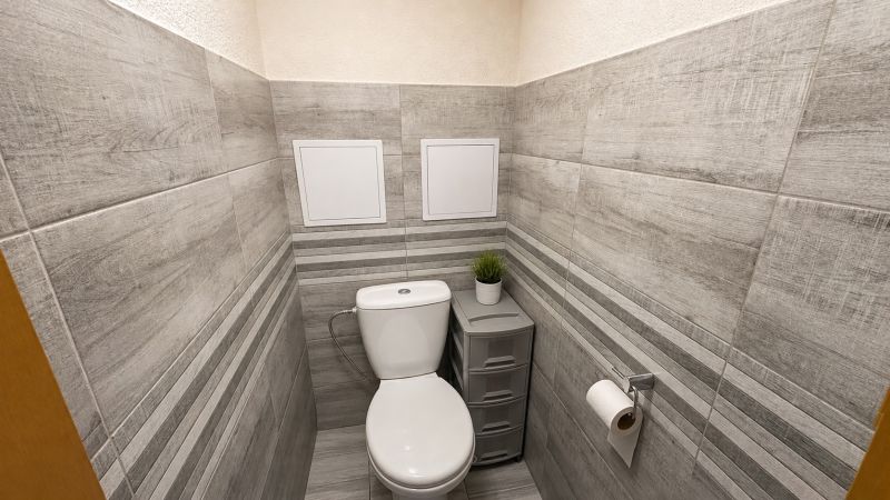 A bathroom with wood-patterned tiles and sanitary ware in a 3-room apartment.
