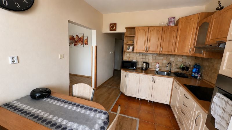 A kitchen in a 3-room apartment with wooden decor on the floor and wooden cabinets.