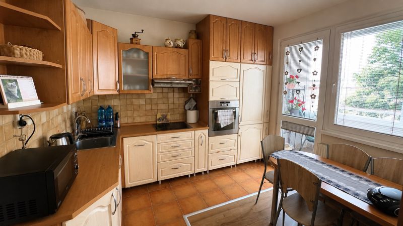 A kitchen in a 3-room apartment with light furniture and a wooden decor floor.
