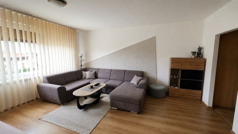 Living room with a corner sofa, table, and wooden decor flooring in a 3-room apartment.