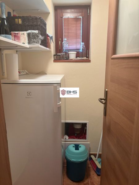 A small room with shelves, a refrigerator, a window, and cleaning equipment in the cottage.