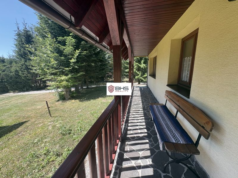 At the Chata na Donovaloch, you can see a stone terrace with a bench and surrounding trees.