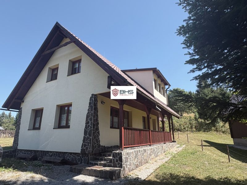A cottage in Donovaly with a slanted roof and stone details on a sunny meadow.