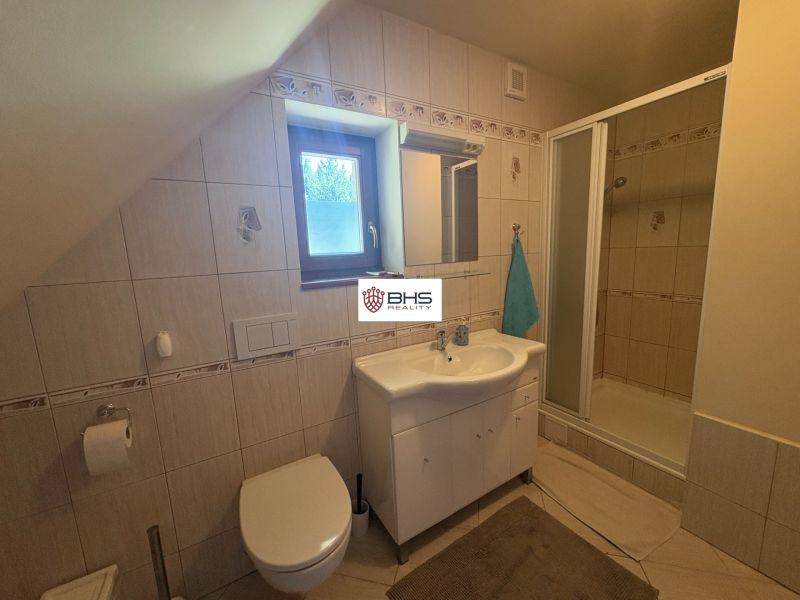 Bathroom in a cottage with a shower, toilet, and sink, light ceramic tiles.