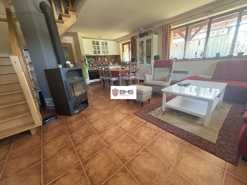 Interior of a cabin with a staircase, seating area, fireplace, kitchen, and wooden decor flooring.