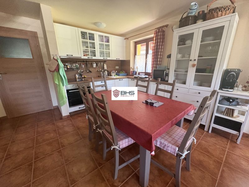 A kitchen in a cottage with white furniture, a dining table, and a terracotta floor.