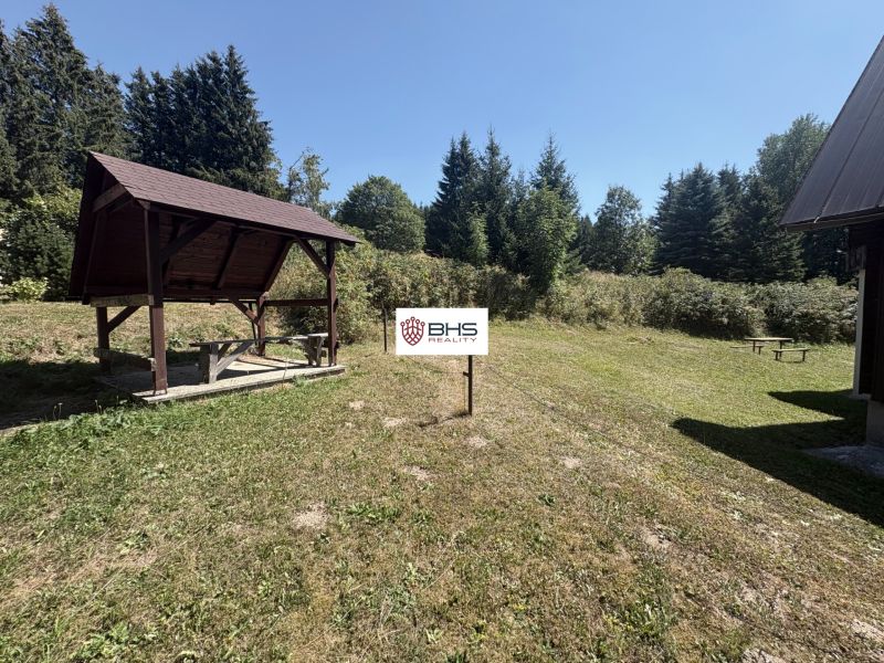 A cottage in Donovaly with a shelter on a grassy yard, lined with trees.