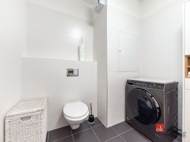 A bathroom in a studio apartment with a washing machine and a wall-mounted toilet.