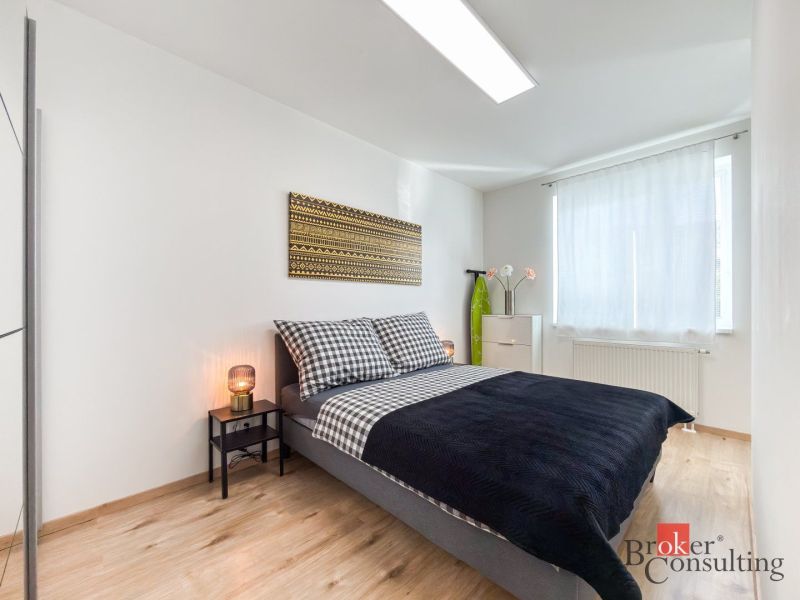 A bedroom with a bed, a nightstand, and a wooden decor floor in a studio apartment.
