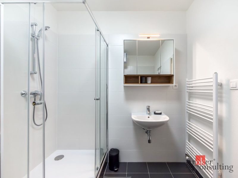 A bathroom with white tiles, a shower corner, and a mirrored cabinet in a studio apartment.