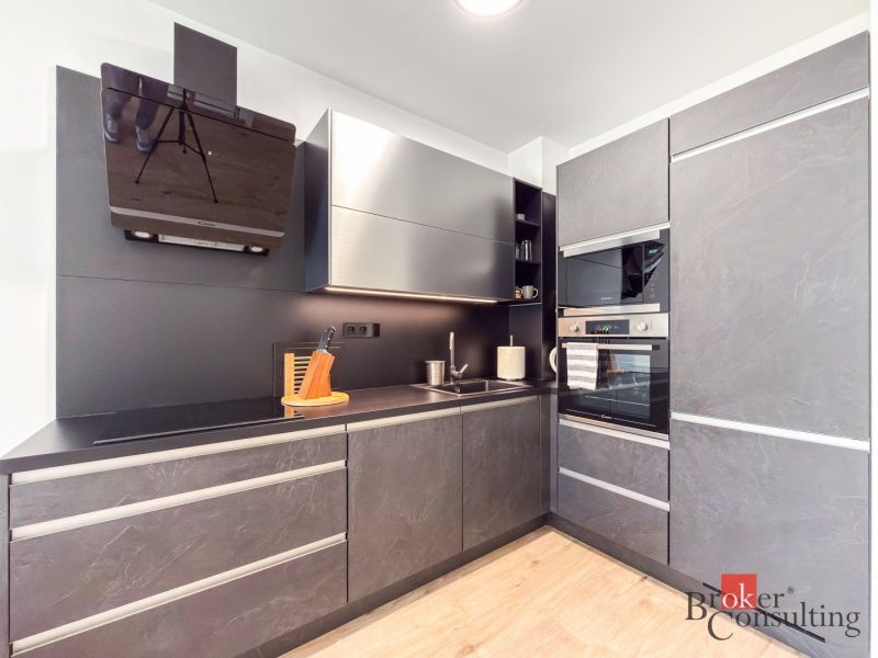 A stylish kitchen in a studio apartment, with black cabinets and a wood-patterned floor.