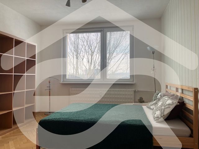 A bedroom with a light wall, a bed, and a floor with a wooden decor in a 3-room apartment.