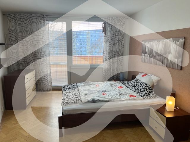 A bedroom in a three-room apartment with a wooden decor floor and balcony doors.