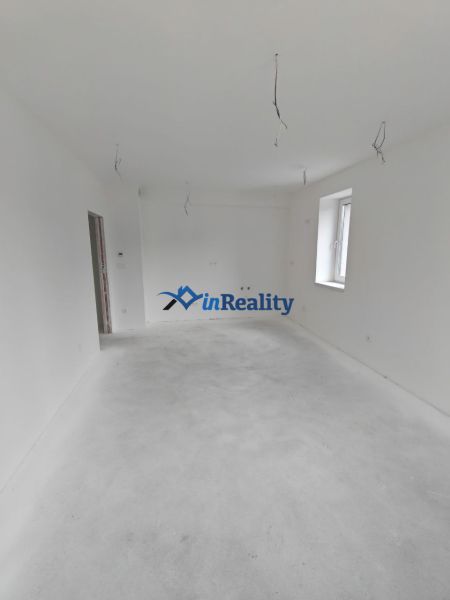 A spacious room in a 2-room apartment with white walls and a large window.
