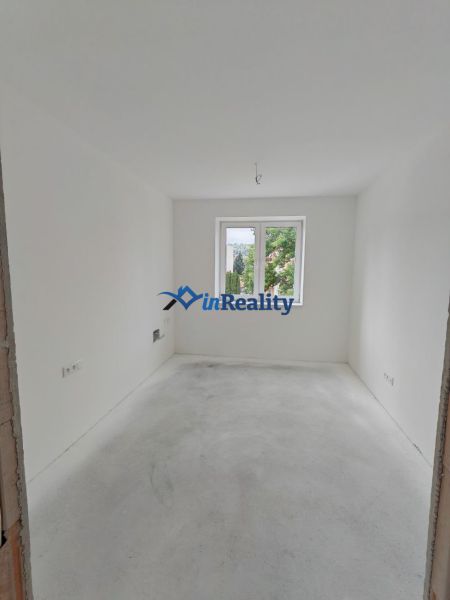 An empty room with white walls and a window in a 2-room apartment without flooring.