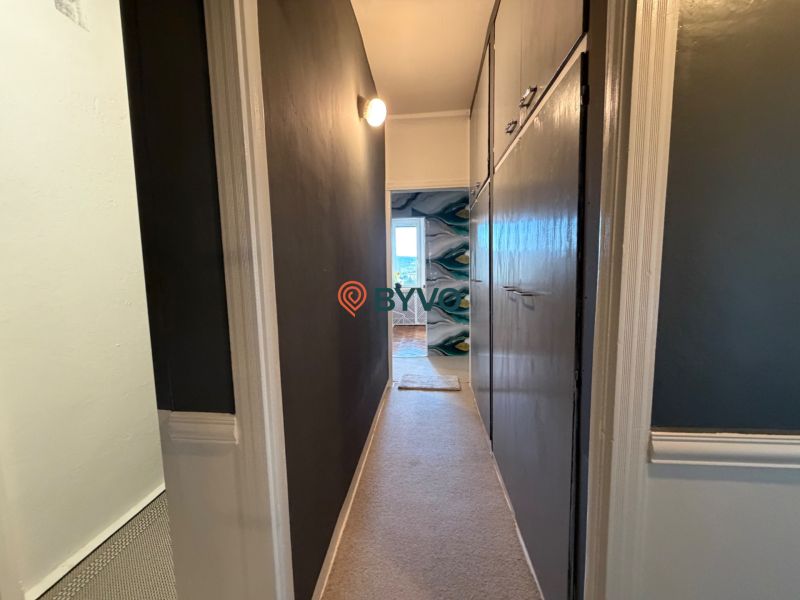 A narrow hallway leading to a room with a wooden decor floor in a 4-room apartment.