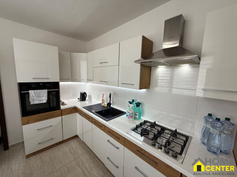 A kitchen in a 3-room apartment with white cabinets and appliances, and a wooden decor floor.
