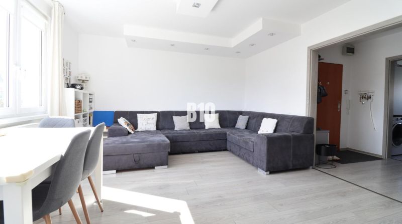 Living room in a 3-room apartment with a sofa, dining area, and wooden decor flooring.