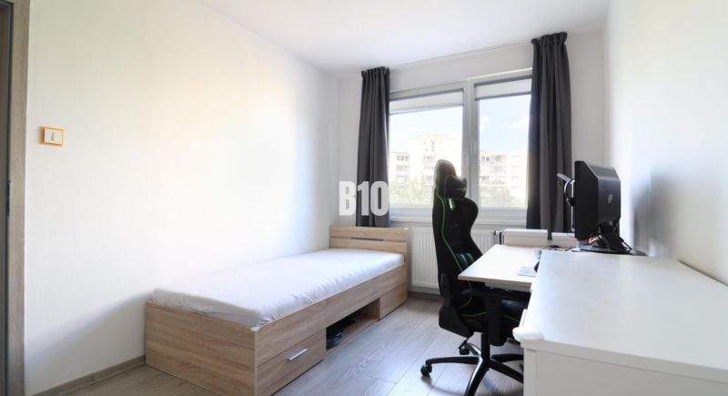 A room in a 3-room apartment with a bed, a computer desk, and a floor with a wooden decor.