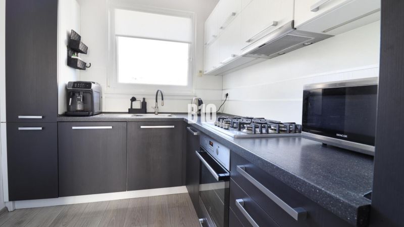 A kitchen with a stove, microwave, and coffee maker in a 3-room apartment, with a wooden decor floor.