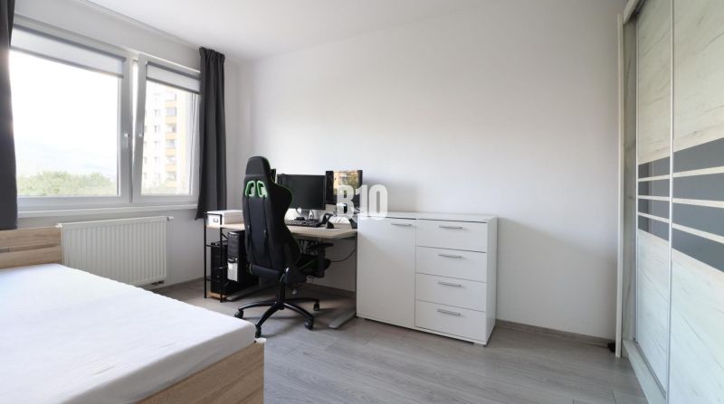 A room in a 3-room apartment with a spacious window, a desk, and a floor with a wooden decor.