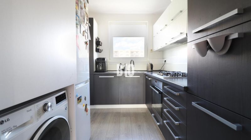 A kitchen with a washing machine and appliances in a 3-room apartment, floor with wood decor.