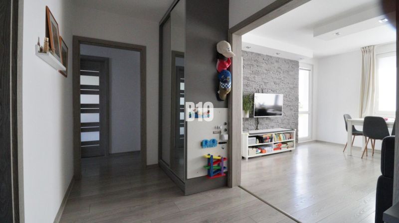 Interior of a 3-room apartment with wood-patterned flooring, a living room wall unit, and a dining table.