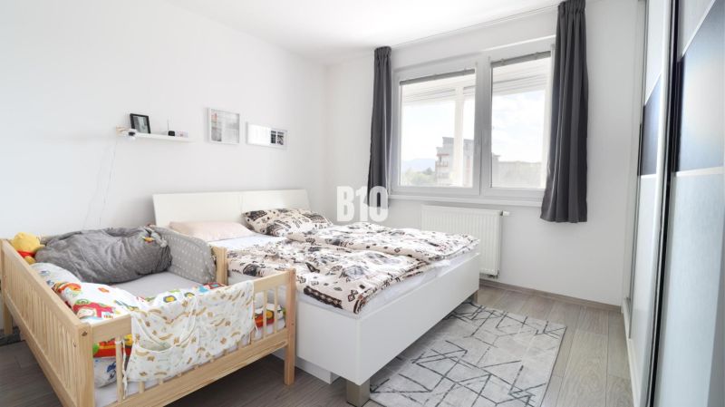 Bedroom in a 3-room apartment with a bed, a baby crib, and a floor with a wooden decor.