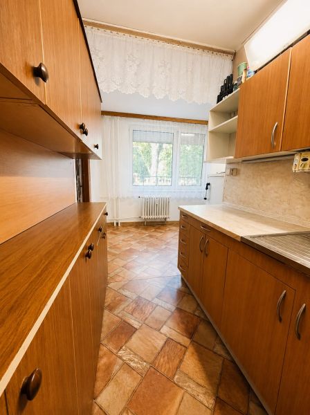 A kitchen in a 3-room apartment with a wooden decor floor and curtains.