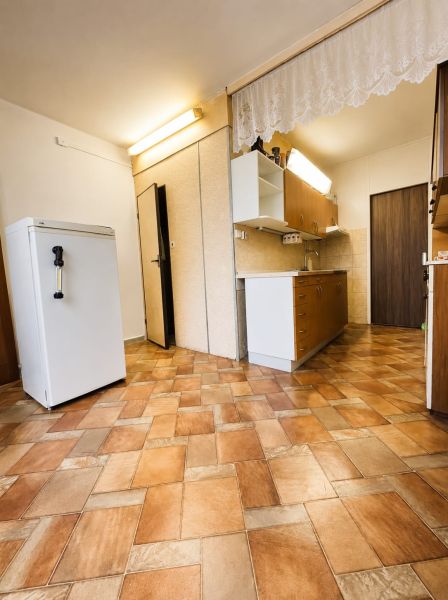 A kitchen in a 3-room apartment with wood-patterned tiles, cabinets, and a refrigerator.