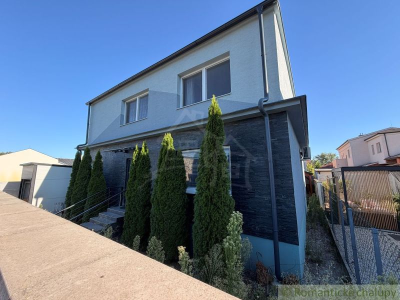 A family house in Komárno with a modern facade and a row of cypress trees in front of the entrance.