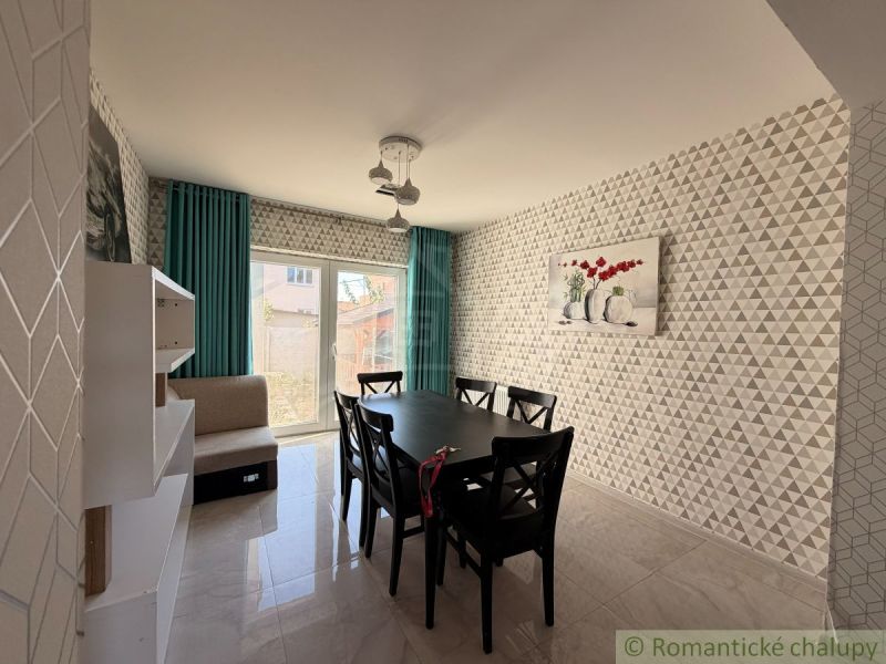 A dining room in a family house with geometric wallpaper, a black table, and turquoise curtains.
