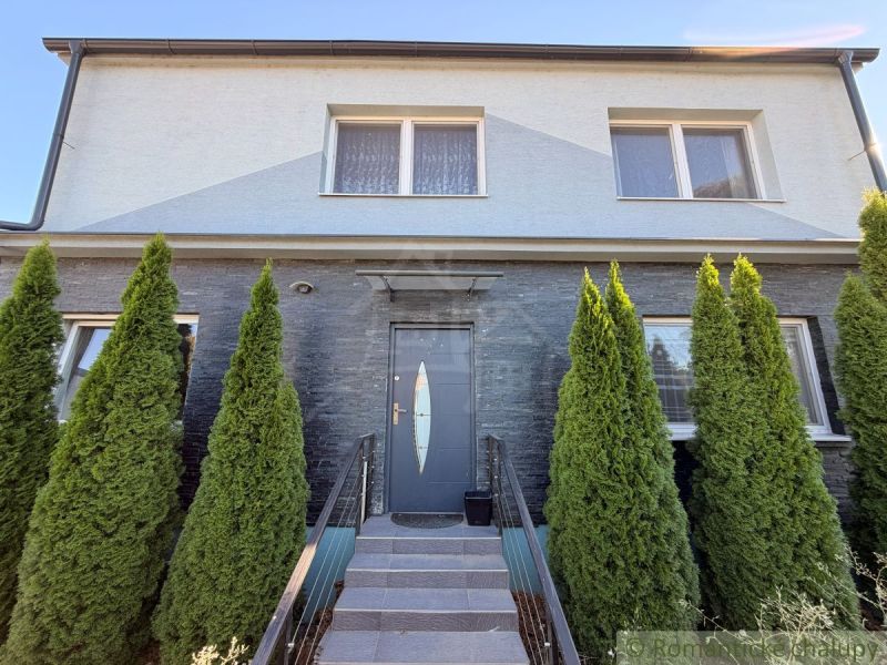 A family house in Komárno with a gray facade and thuja trees in front of the entrance.