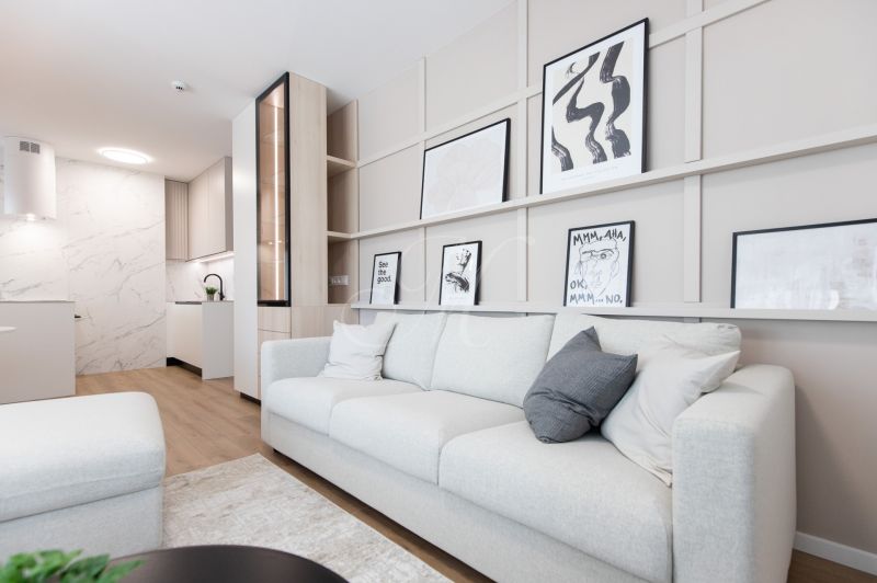 Living room of a two-room apartment with wood-patterned flooring, a sofa, and modern art.