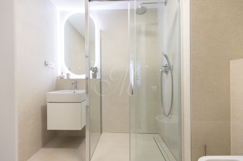 A bathroom in a 2-room apartment with a modern shower and an illuminated mirror.