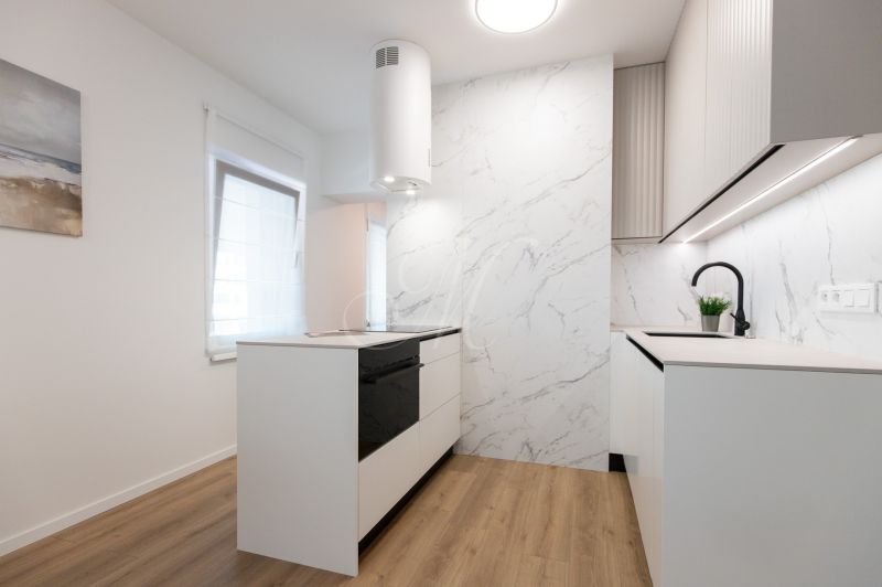 A kitchen in a 2-room apartment with a light-colored kitchenette, beige wall, and a floor with a wood decor.