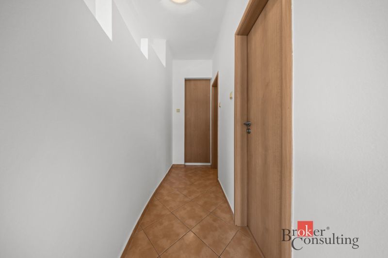 A hallway with white walls, brown floor, and doors in a 2-room apartment.