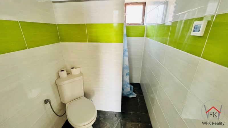 Bathroom in a family house with green and white tiles and a toilet.