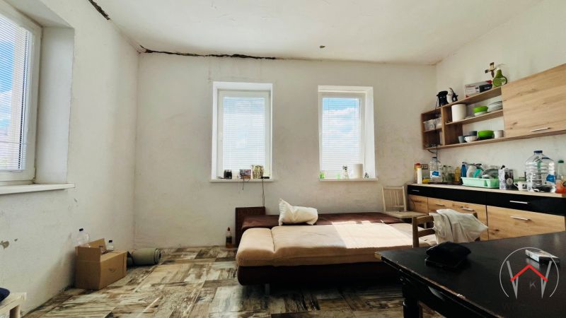 A room in a family house with a kitchen unit, wooden decor flooring, and a sofa.