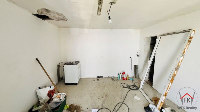 A room in a family house with clutter, a stove, and repairs on the ceiling and floor.