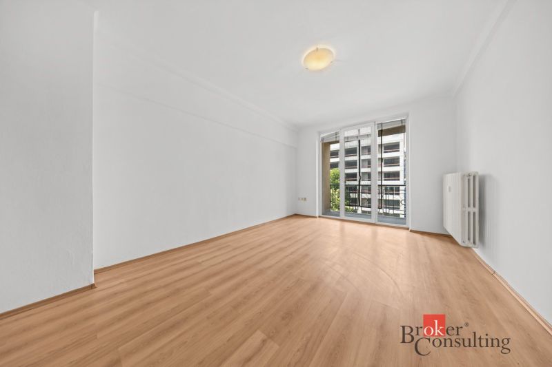 A bright room with wood-patterned flooring and balcony doors in a 2-room apartment.