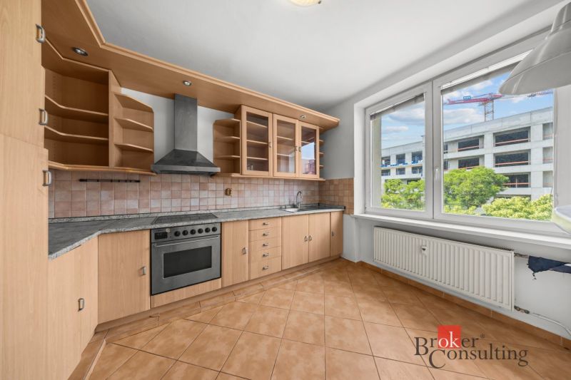 A kitchen in a 2-room apartment with tiles, a wooden kitchen unit, and a large window.