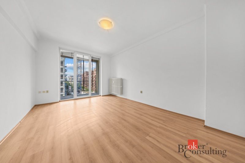 A bright room in a 2-room apartment with a wooden decor floor and balcony doors.