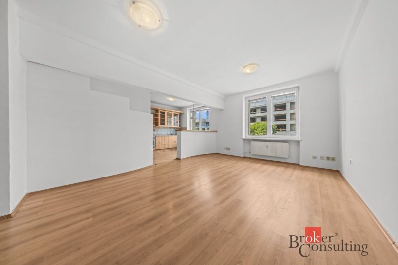 Living room with wood-patterned flooring connected to the kitchen in a 2-room apartment.